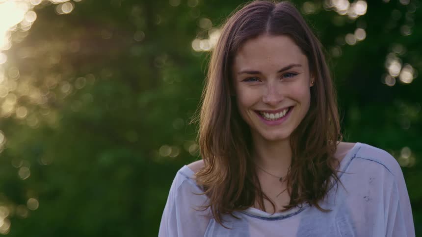A young woman smiles and laughs into the camera while standing outdoors