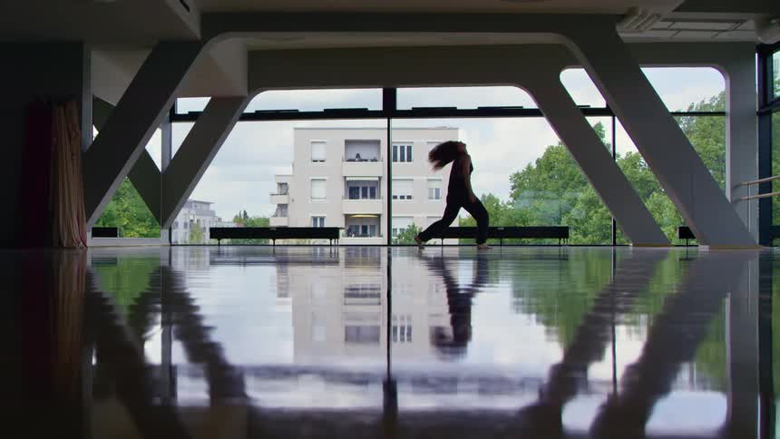 A woman does a modern dance under a bridge next to a river in a city