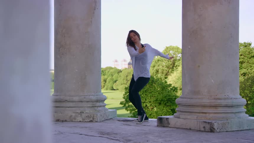 A woman is dancing near the large pillars