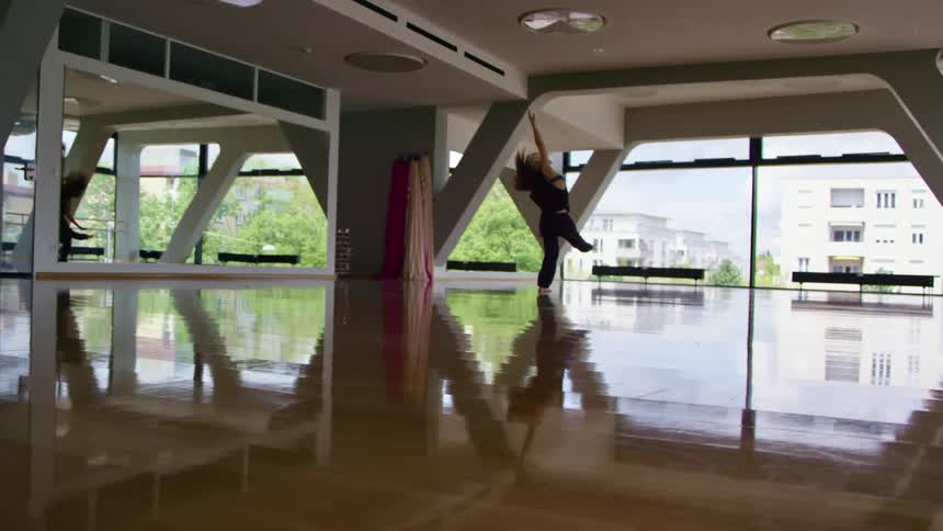 A woman practices a modern dance in a studio with reflective wood floors