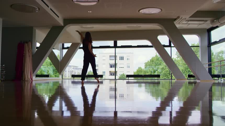 A woman in a room dancing and spinning with windows in the background