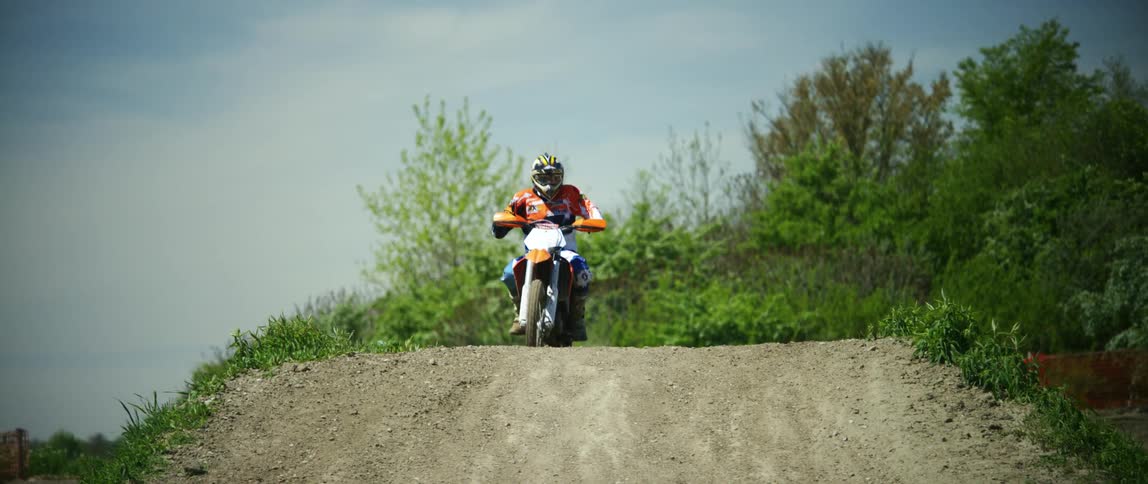Man drives an off road dirt bike over the slope of a dirt track