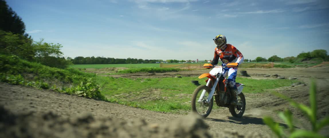 A man with a helmet riding a dirt bike on an obstacle course with the sky and clouds in the background