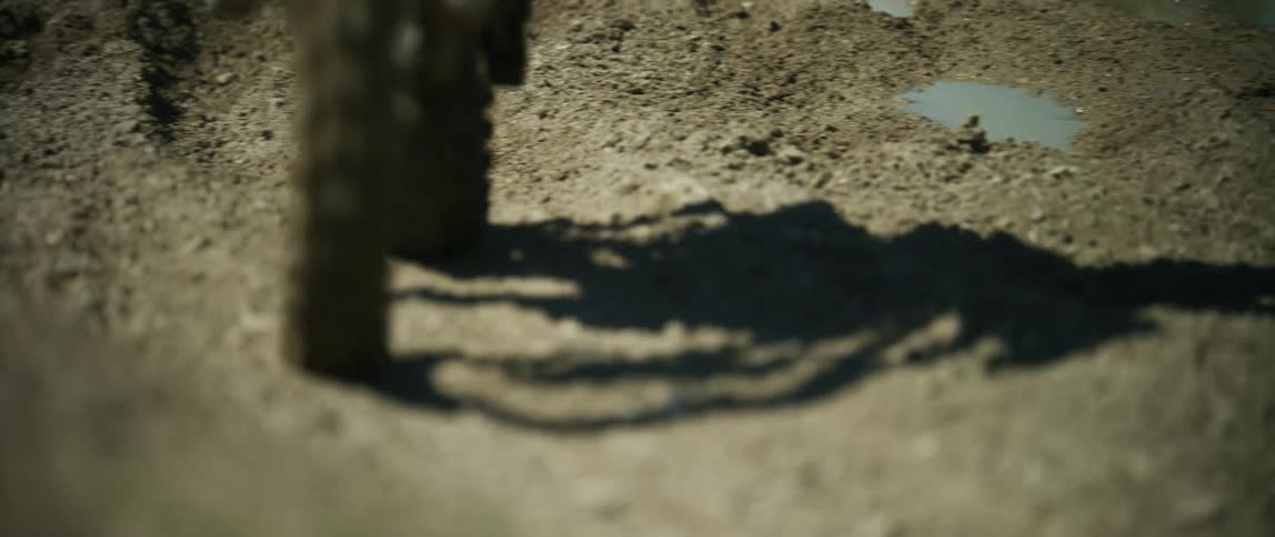 A person rides a dirt bike along a dirt road covered in dents and puddles