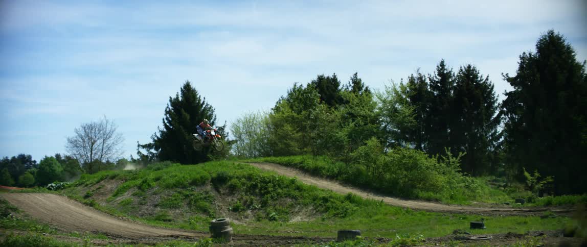 A person with a helmet riding a dirt bike on an obstacle course with the sky and clouds in the background