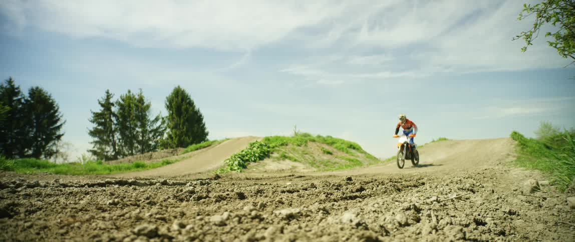 Man rides a motocross motorcycle on a dirt road jumping over a slope