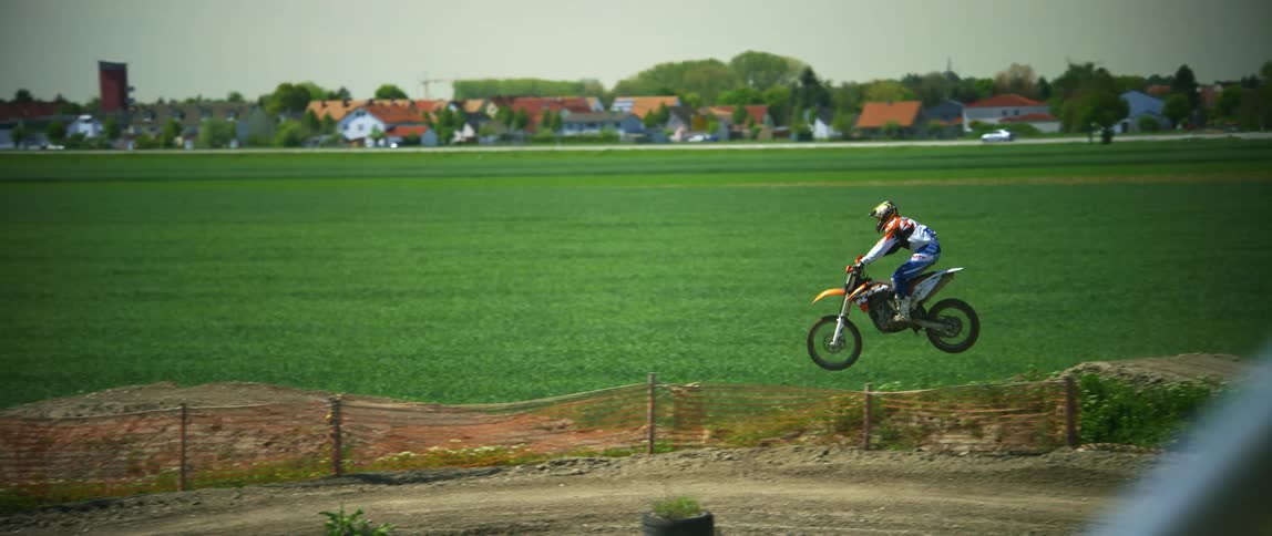 A motorcyclist rides a dirt bike over a set of dirt hills on an offroad motorcycle track