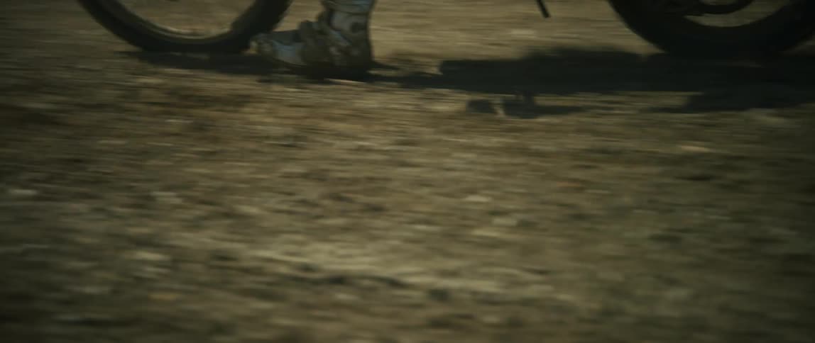 Person rides motorcycle along muddy dirt road past field