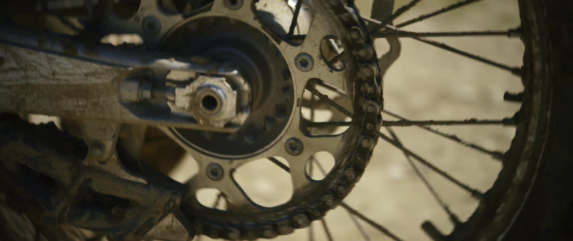 The wheel of a dirt bike is caked in mud as the rider gradually accelerates and drives away