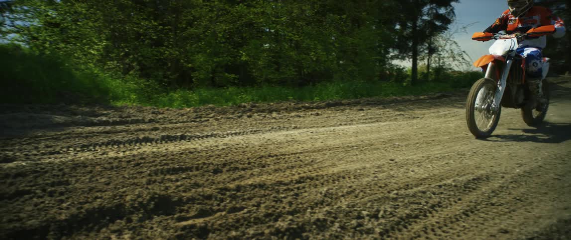 A motocross rider rides down a dirt trail and through a puddle