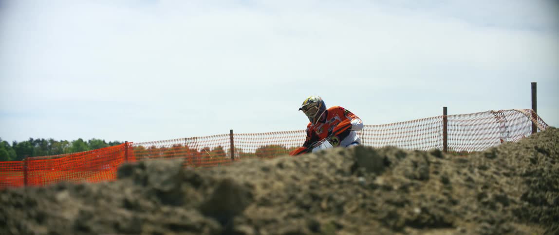 Man wearing protective gear drives a dirt bike on a motocross track outdoors