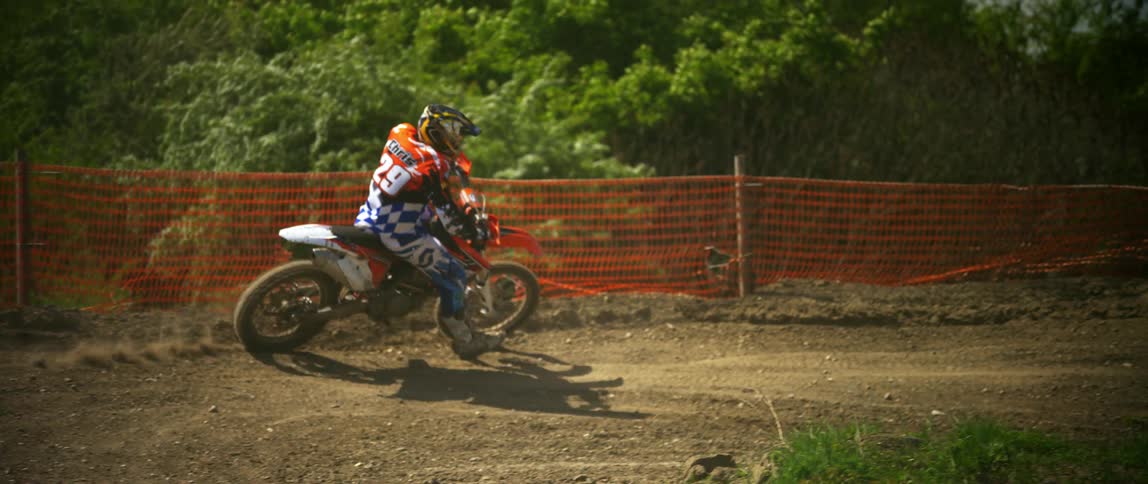 A person with a helmet riding a dirt bike with trees and the sky in the background