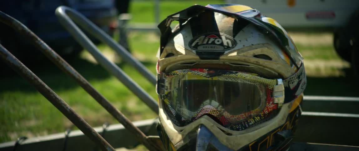 Off road motocross helmet with visor and goggles over the back of a rack outdoors