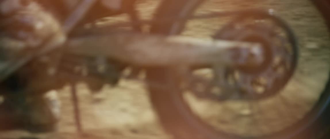 A motocross rider in full personal protective equipment rides a dirt bike around a corner on a dirt track