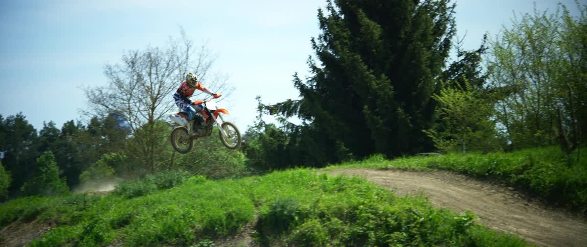 A person on a dirt bike get airborne while going over an incline on a dirt race track