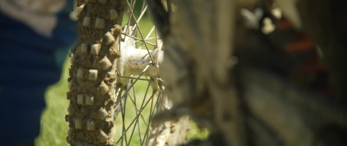 Person pushes mud crusted bicycle over grass