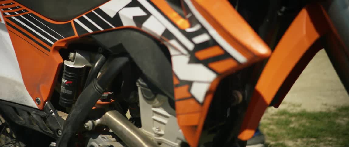 A person with a helmet sitting on a dirt bike with the sky and clouds in the background