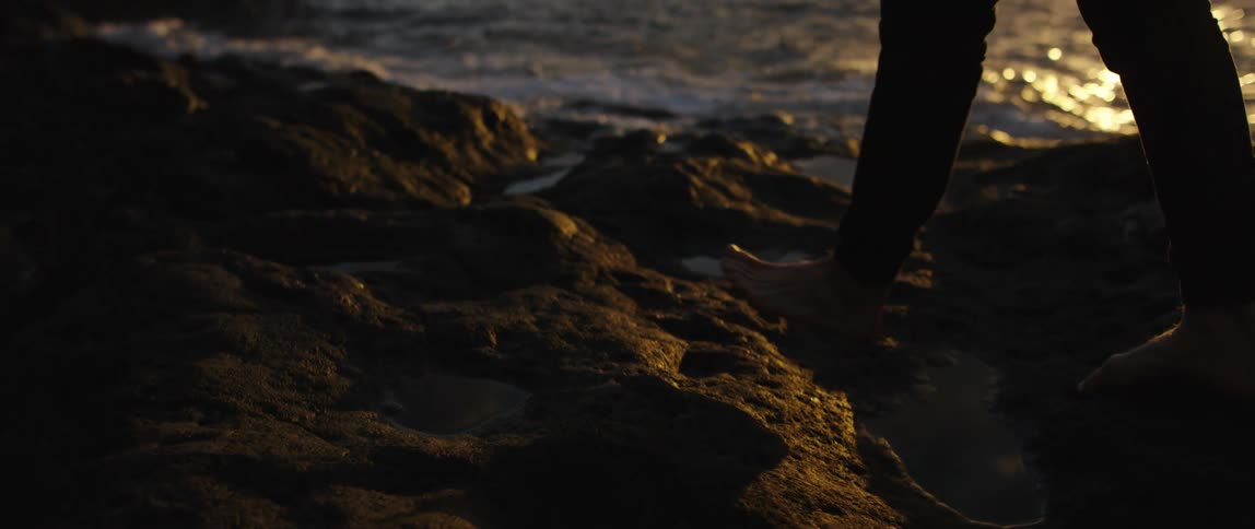 A man walks barefoot along rocks on the coast near the ocean