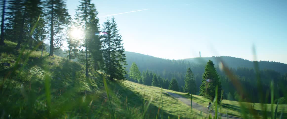 Two cyclist ride bicycles on a dirt road with green hills and mountains in the background