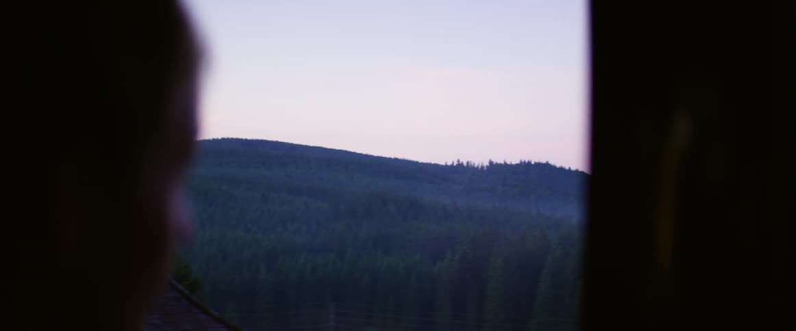 A person opens a curtain to look at the mountains and forests at sunset