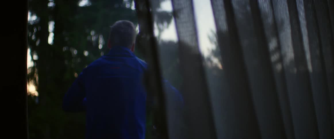 Man standing outside of window with curtain puts on jacket at sunrise