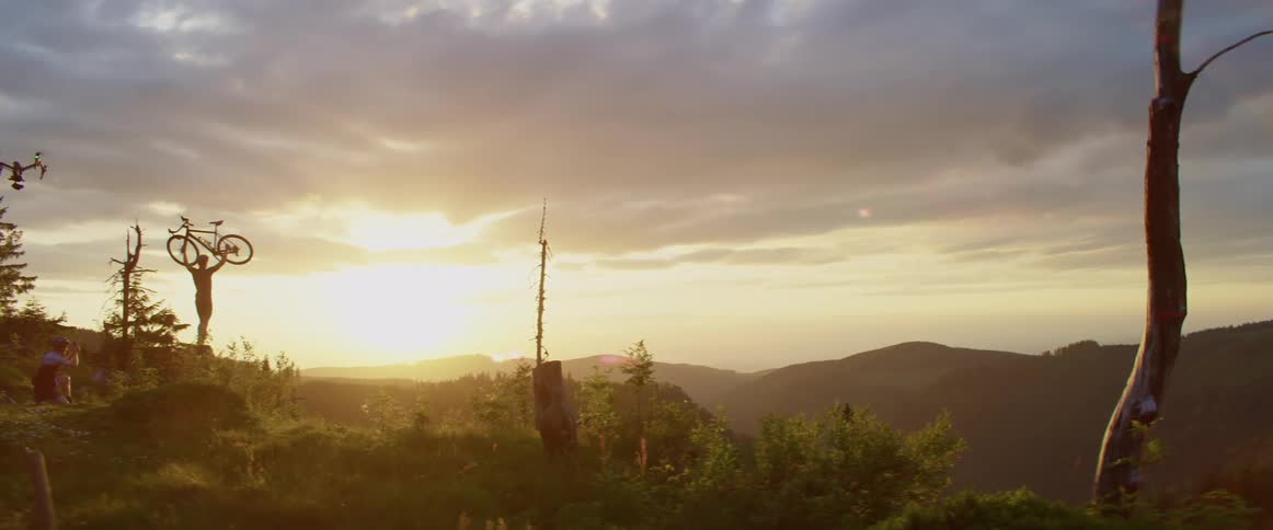 A bicyclist holding up a bicycle in mountains at sunset