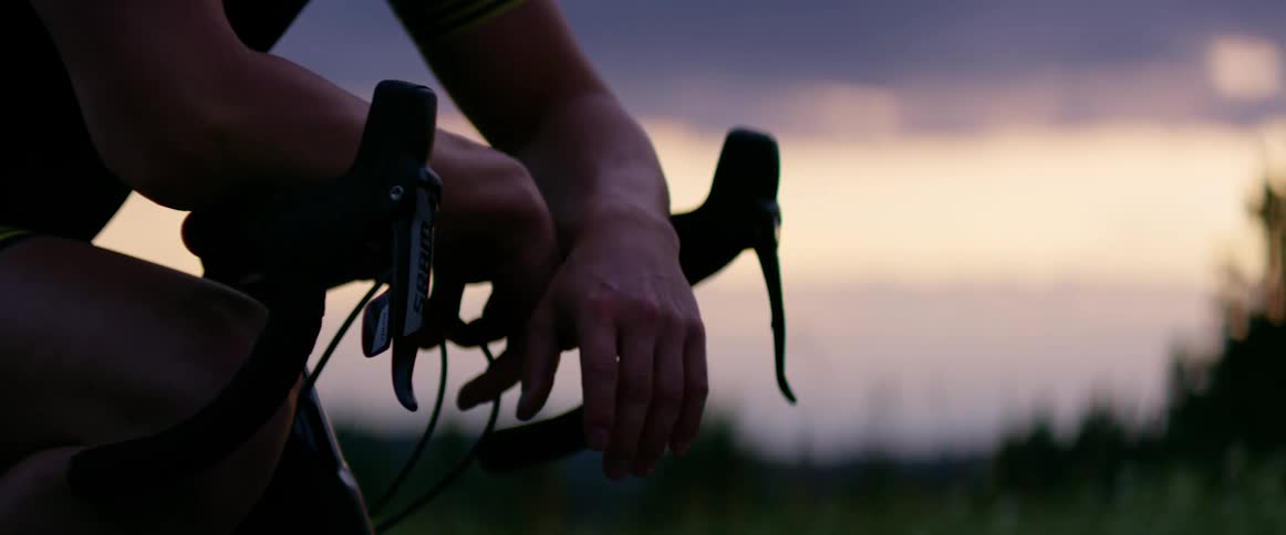 Man reclined on the handlebars of a mountain bike in a field at sunset