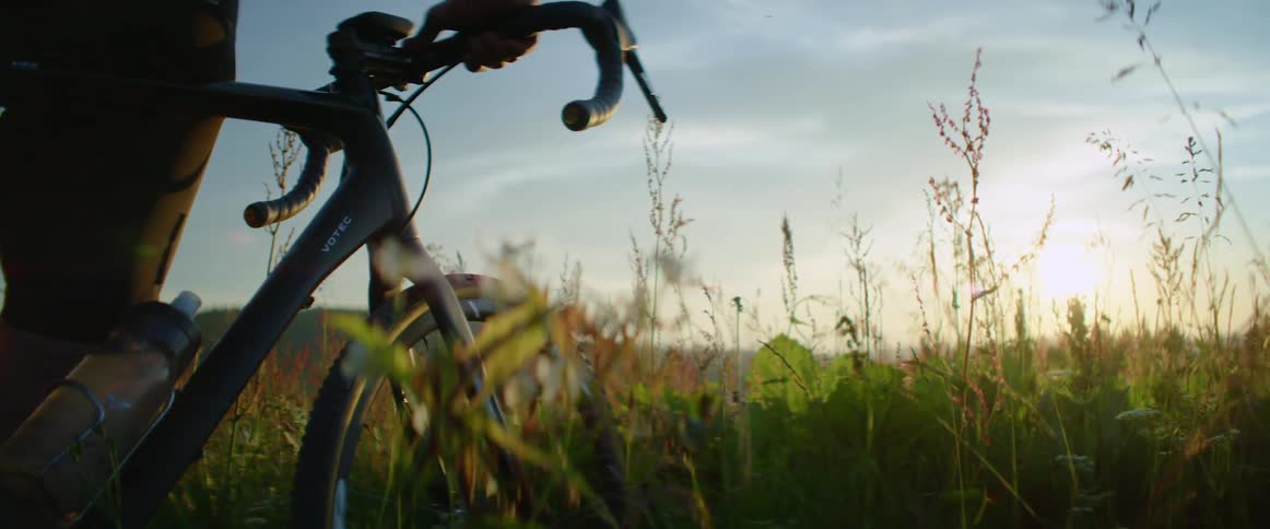 Man stands with a mountain bike on a grass field at sunset
