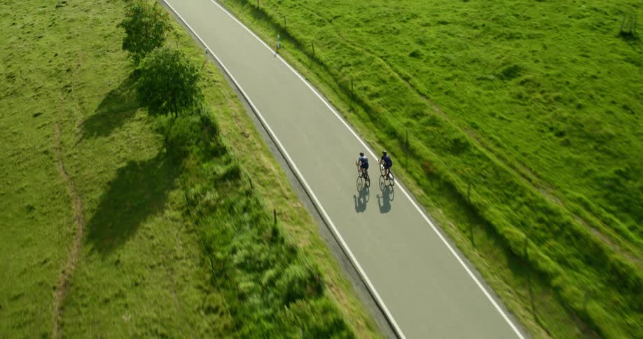 Aerial view of two cyclists riding bicycles on an asphalt road in the countryside