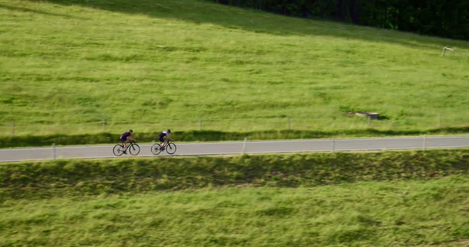 Two cyclists race down a narrow two lane road in a rural area