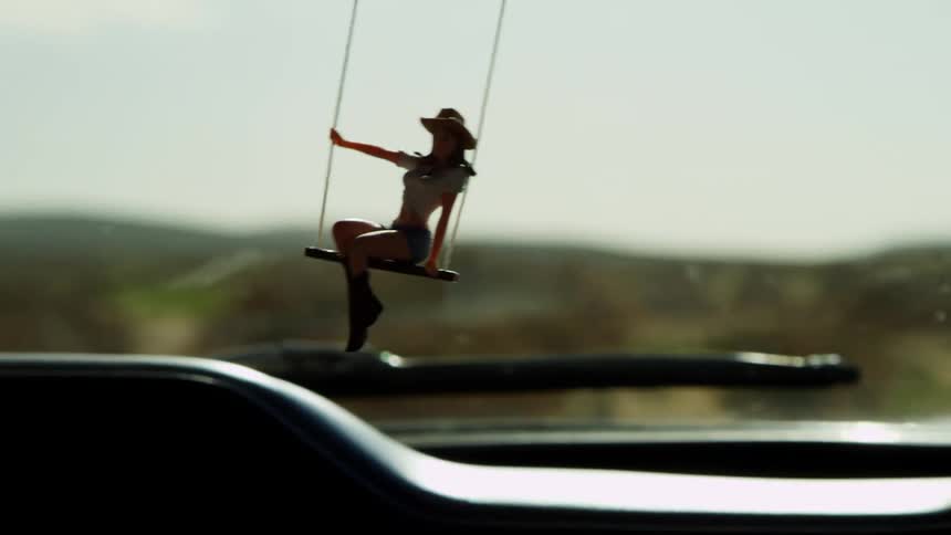 Doll swinging from a rearview mirror of a car driving on a road on the desert