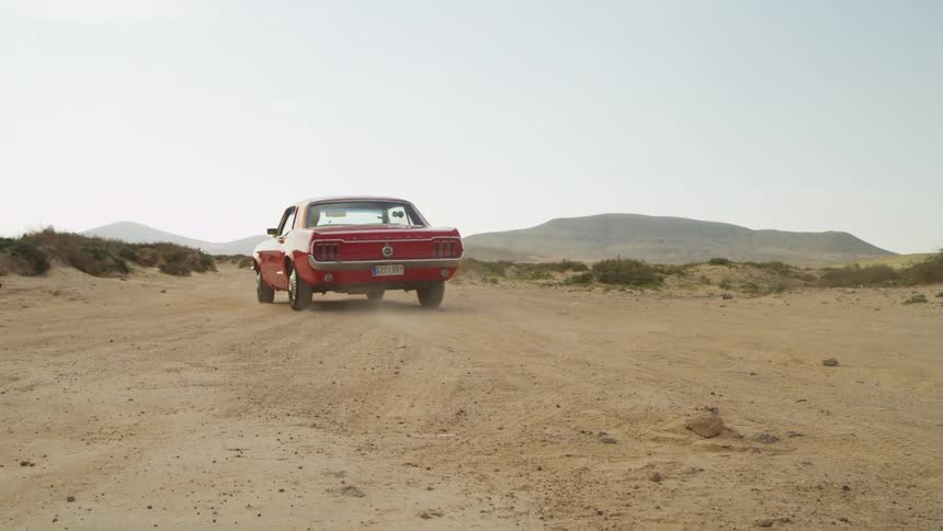 A red antique sports car driving on a rural dirt road in the daytime