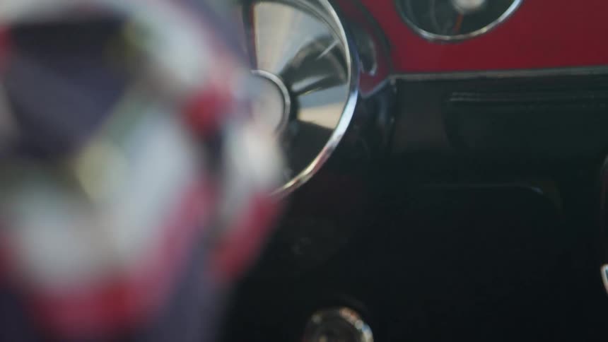 A man in a red plaid shirt drives a vintage vehicle with a red painted dashboard