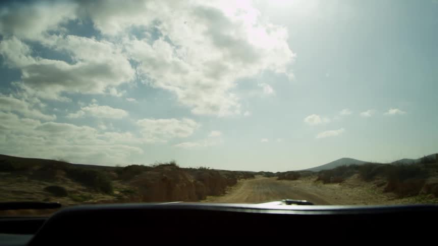 Car driving on a dirt road through the desert at day