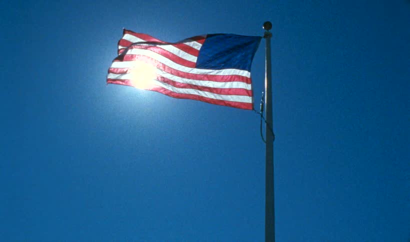 Sunlight flaring through an american flag waving in the wind under a blue sky