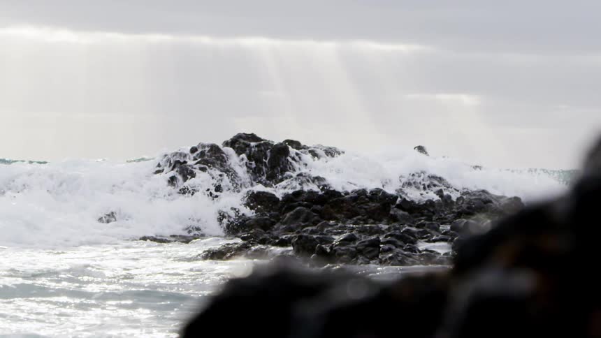 Strong waves crash onto black boulders in the ocean