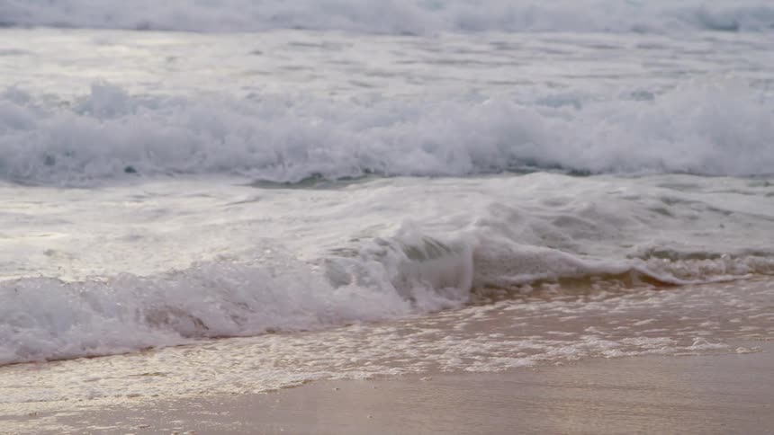 Small waves gently crashing on the sand beach at sunset