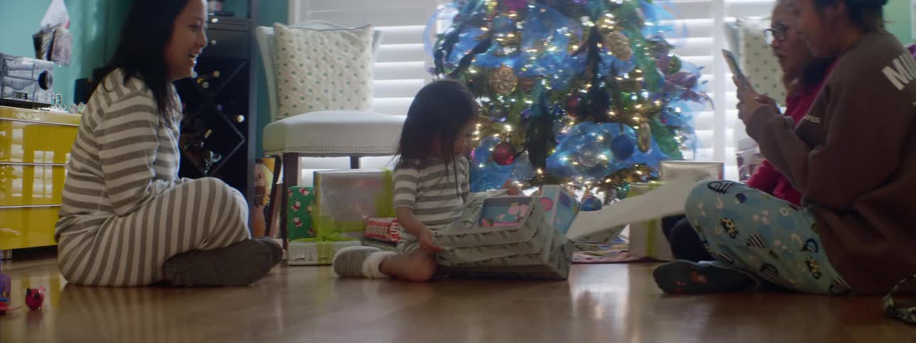 A young girl unwraps a christmas present then joyfully bounces around once she sees the gift itself
