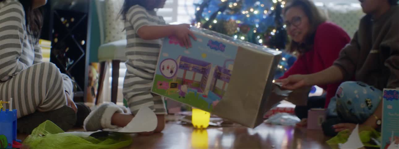 A little girl opens a present in front of a christmas tree and then shows her family what it is