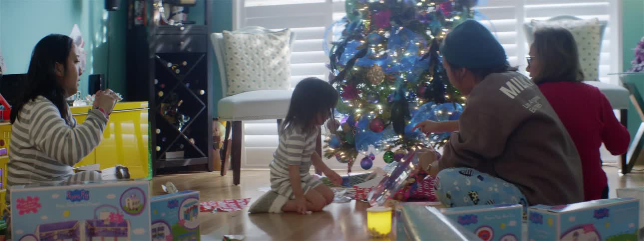 Three women and a little girl next to a christmas tree opening gifts on the floor