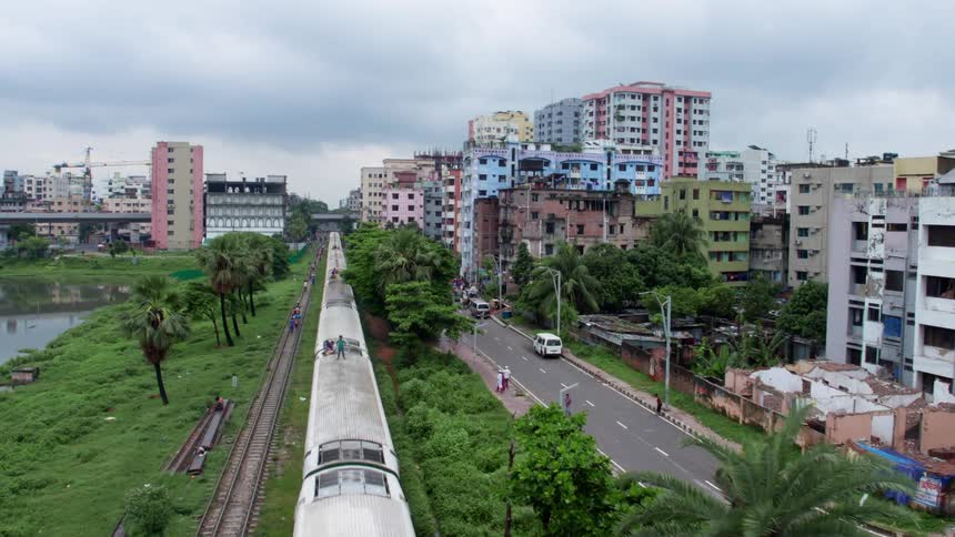 A train traveling through a city in a primitive area while kids walk along the tracks and people walk along the roads