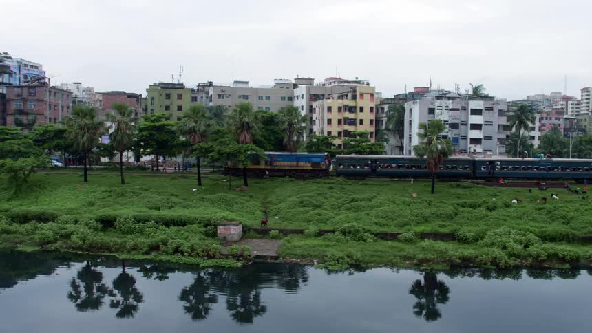Passenger train driving next to a citys residential area close to a river