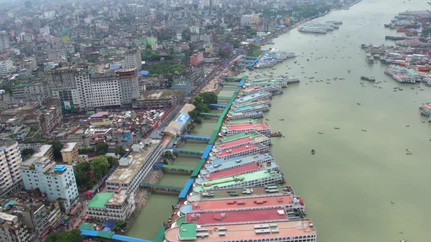 Large colorful boats docked on either side of a murky green river running through a rundown metropolis during the day