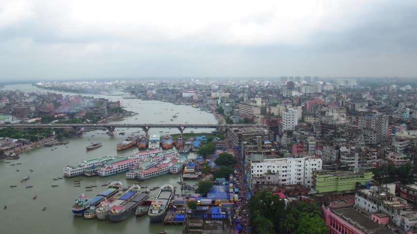 A river crowded with boats and ships runs through a rundown city on a cloudy day