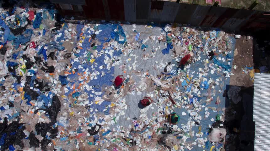 Women sweep garbage on ground as others move across roof near tents