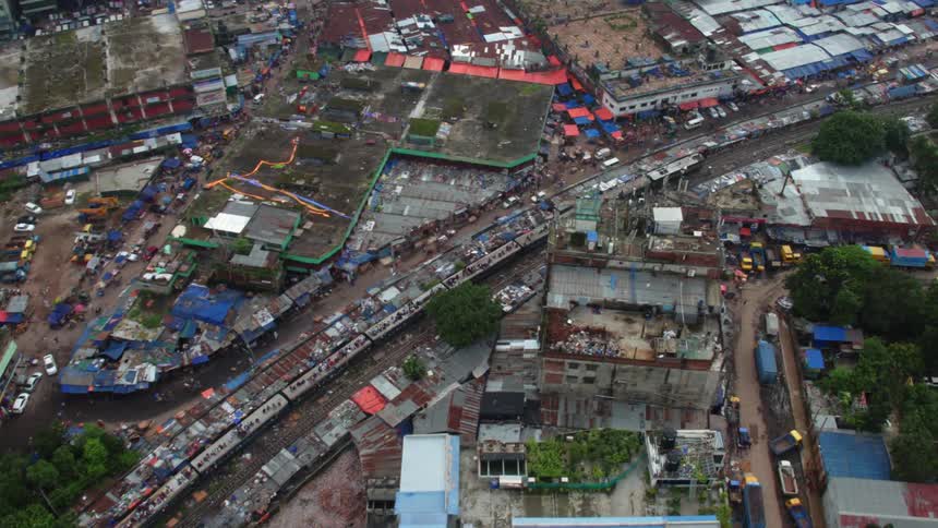 A train with many people riding on its rooftop travel through a rundown city during the day