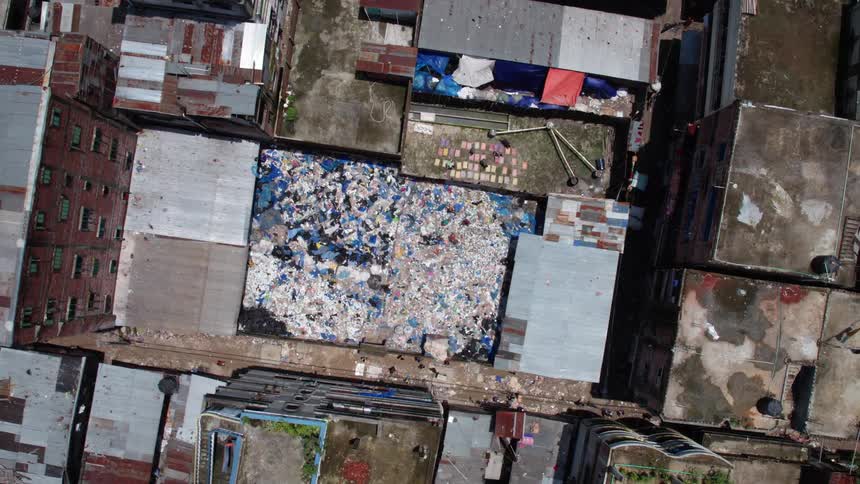 People walking around picking through trash surrounded by buildings
