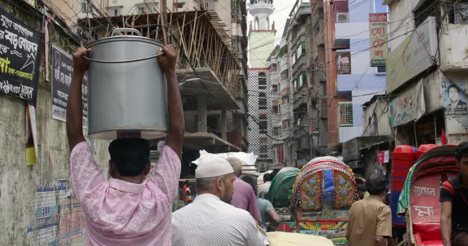A man carries a large pot atop his head as he walks down an extremely crowded city street during the day
