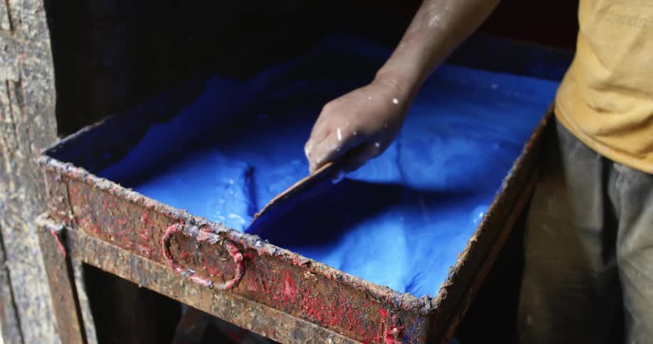 A person mixing blue paint in a tray