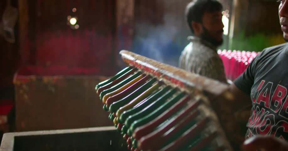 A factory worker lifts a tray holding color plastic tubes from a large vat of liquid